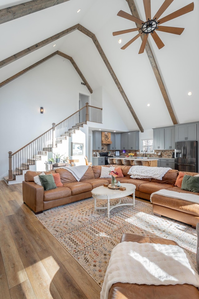 living room featuring sink, beam ceiling, light hardwood / wood-style floors, and high vaulted ceiling