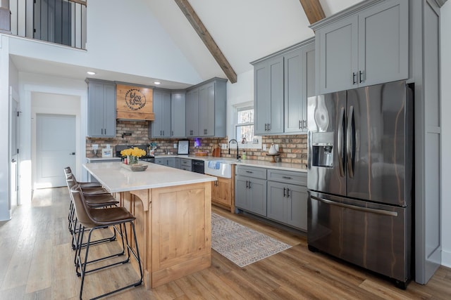 kitchen featuring a breakfast bar area, appliances with stainless steel finishes, high vaulted ceiling, a center island, and beamed ceiling