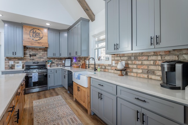 kitchen featuring sink, vaulted ceiling with beams, light stone countertops, stainless steel gas range, and light wood-type flooring