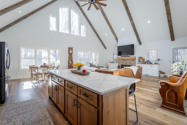 kitchen featuring refrigerator, high vaulted ceiling, a kitchen breakfast bar, a center island, and a brick fireplace