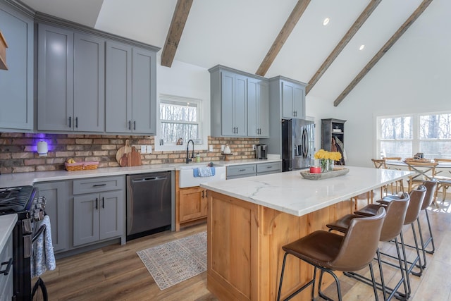 kitchen featuring a center island, stainless steel appliances, beam ceiling, light stone countertops, and decorative backsplash