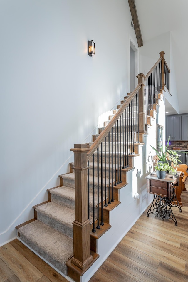 staircase featuring hardwood / wood-style flooring, beamed ceiling, and a high ceiling