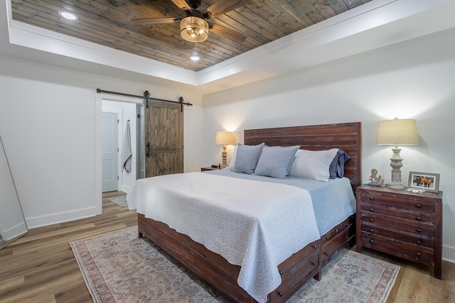 bedroom with wood-type flooring, wooden ceiling, a raised ceiling, ceiling fan, and a barn door