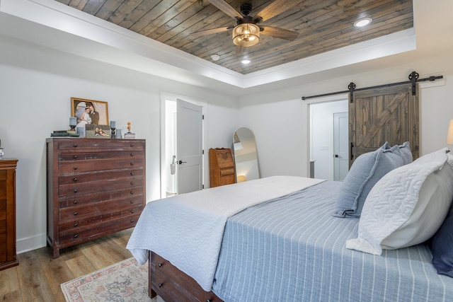 bedroom featuring ceiling fan, a raised ceiling, a barn door, wooden ceiling, and light hardwood / wood-style flooring