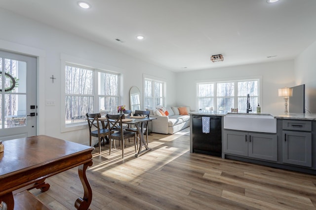 kitchen with sink, light stone counters, gray cabinets, black dishwasher, and light hardwood / wood-style floors