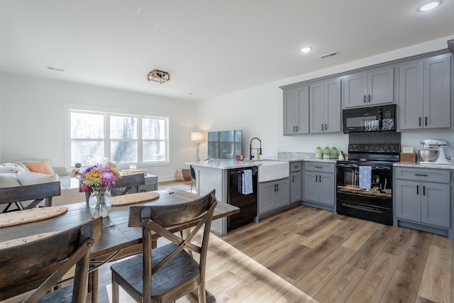 kitchen with sink, gray cabinets, kitchen peninsula, light hardwood / wood-style floors, and black appliances