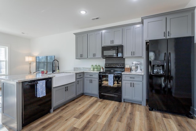 kitchen with sink, light hardwood / wood-style flooring, black appliances, and kitchen peninsula