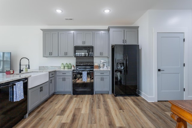 kitchen featuring sink, light stone counters, light wood-type flooring, gray cabinets, and black appliances