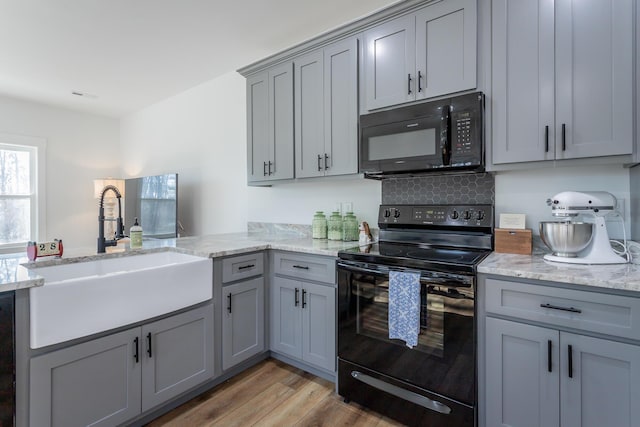 kitchen featuring sink, gray cabinetry, light stone countertops, light hardwood / wood-style floors, and black appliances