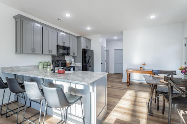 kitchen with black appliances, gray cabinetry, dark hardwood / wood-style flooring, decorative backsplash, and kitchen peninsula