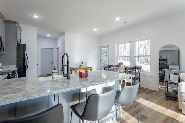 kitchen with gray cabinets, light stone countertops, light hardwood / wood-style floors, and black appliances