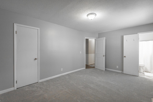 unfurnished bedroom with ensuite bathroom, light colored carpet, and a textured ceiling