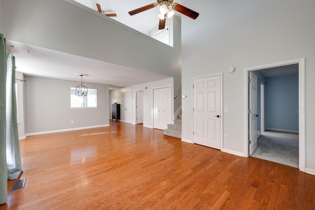 unfurnished living room featuring a towering ceiling, light hardwood / wood-style floors, and ceiling fan with notable chandelier