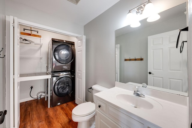 bathroom featuring wood-type flooring, vanity, stacked washing maching and dryer, and toilet