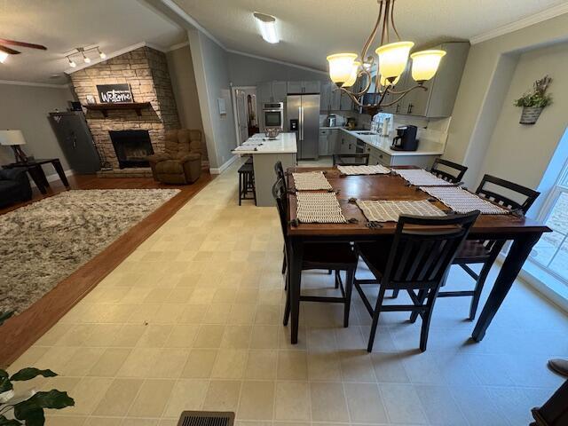 dining area featuring ceiling fan with notable chandelier, crown molding, lofted ceiling, and a stone fireplace