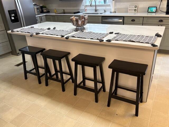 kitchen with gray cabinetry, a breakfast bar, a center island, sink, and stainless steel appliances