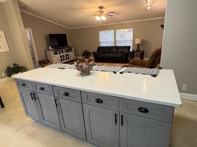 kitchen with gray cabinetry, crown molding, vaulted ceiling, ceiling fan, and light stone counters