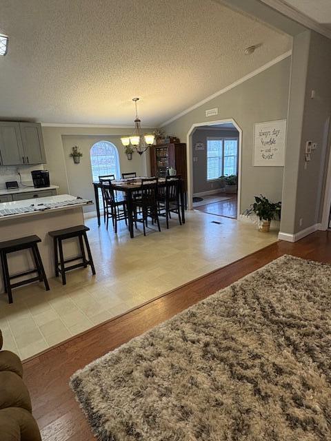 dining space with light wood-type flooring, ornamental molding, a textured ceiling, vaulted ceiling, and an inviting chandelier