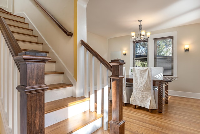 stairs featuring wood-type flooring and an inviting chandelier