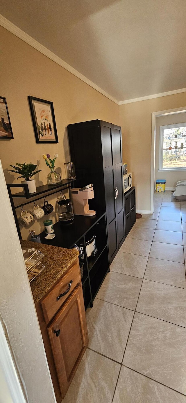 kitchen featuring light tile patterned floors, crown molding, and dark stone counters