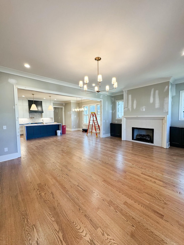 unfurnished living room featuring a tile fireplace, light hardwood / wood-style flooring, a chandelier, and ornamental molding