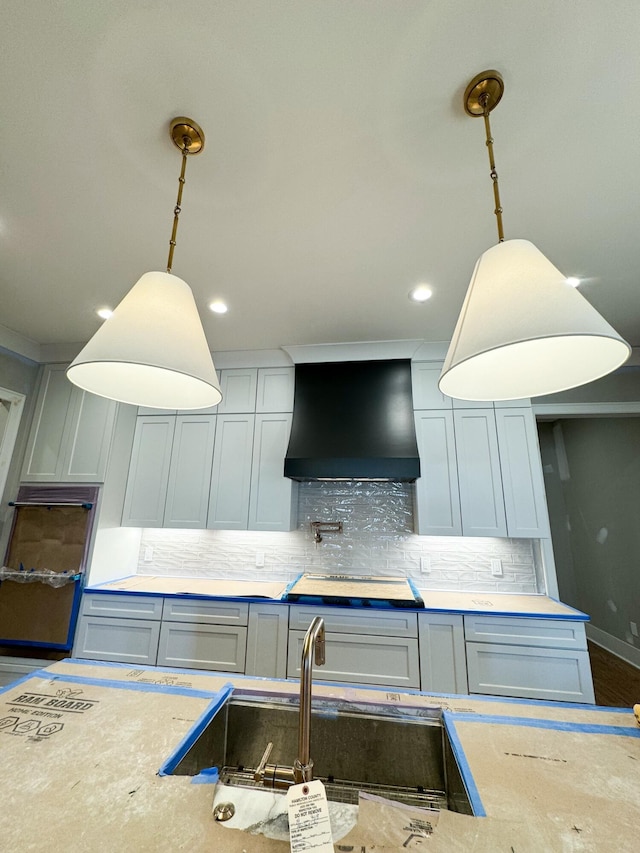 kitchen featuring custom range hood, tasteful backsplash, hanging light fixtures, and sink