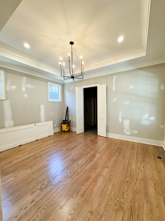 interior space with light wood-type flooring, a tray ceiling, and a notable chandelier