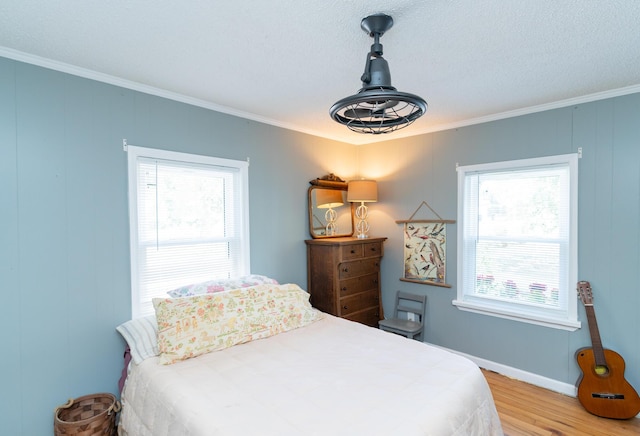 bedroom featuring light wood-type flooring, ornamental molding, a textured ceiling, and multiple windows