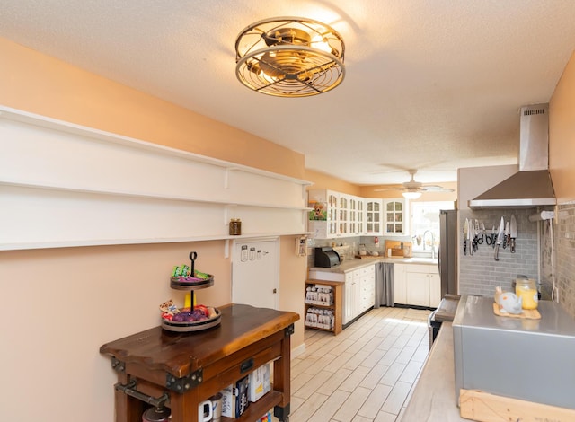 kitchen with ceiling fan, white cabinetry, a textured ceiling, and wall chimney range hood