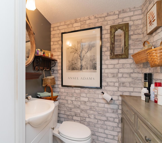 bathroom with vanity, toilet, a textured ceiling, and brick wall