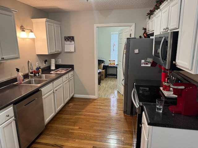 kitchen with white cabinetry, sink, wood-type flooring, a textured ceiling, and appliances with stainless steel finishes