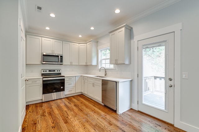 kitchen featuring sink, stainless steel appliances, crown molding, decorative backsplash, and light wood-type flooring