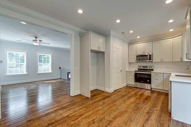 kitchen with sink, hardwood / wood-style flooring, ceiling fan, ornamental molding, and appliances with stainless steel finishes