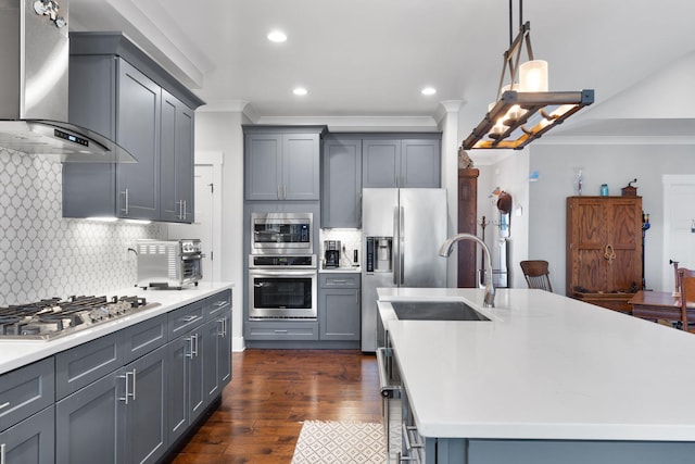 kitchen featuring appliances with stainless steel finishes, backsplash, wall chimney exhaust hood, gray cabinetry, and a kitchen island with sink