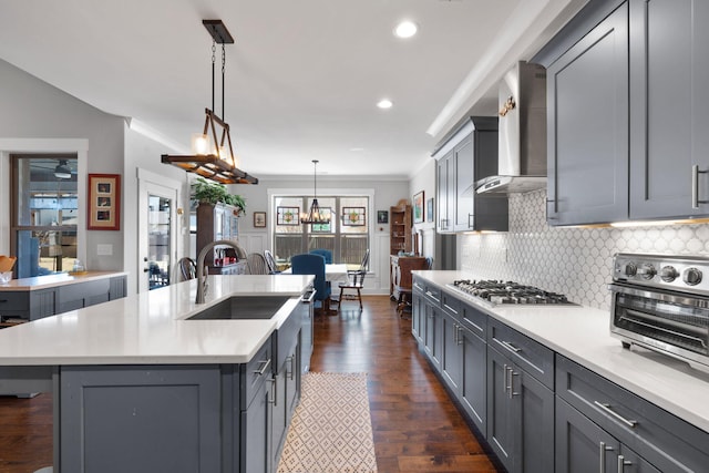 kitchen with wall chimney exhaust hood, stainless steel gas cooktop, a kitchen island with sink, decorative light fixtures, and gray cabinets