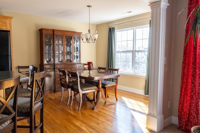 dining space with ornate columns, light hardwood / wood-style floors, and an inviting chandelier