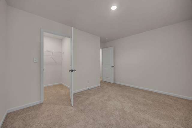 unfurnished bedroom featuring a walk in closet, a closet, and light colored carpet