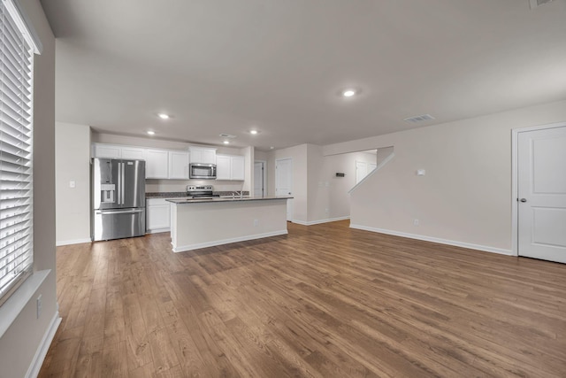 kitchen with hardwood / wood-style floors, white cabinets, an island with sink, and appliances with stainless steel finishes