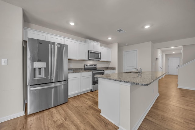 kitchen with dark stone countertops, white cabinetry, a kitchen island with sink, and appliances with stainless steel finishes