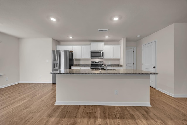 kitchen with appliances with stainless steel finishes, a kitchen island with sink, sink, light hardwood / wood-style flooring, and white cabinetry