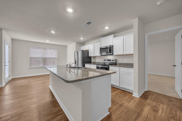 kitchen with dark stone countertops, white cabinetry, an island with sink, and appliances with stainless steel finishes