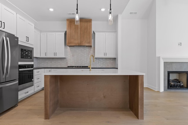 kitchen featuring light wood-style floors, appliances with stainless steel finishes, decorative backsplash, and a tile fireplace