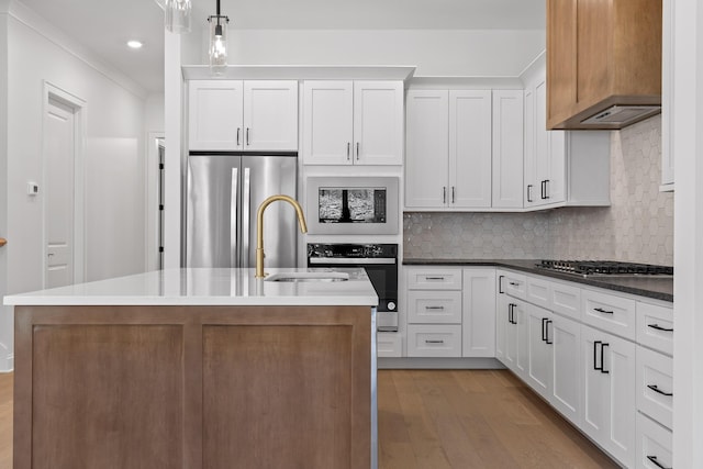 kitchen featuring light wood-style flooring, appliances with stainless steel finishes, tasteful backsplash, a center island with sink, and pendant lighting