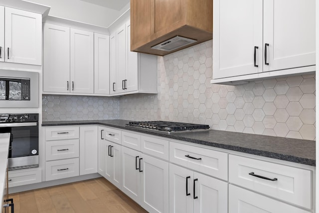 kitchen with white cabinets, decorative backsplash, dark countertops, custom range hood, and stainless steel appliances