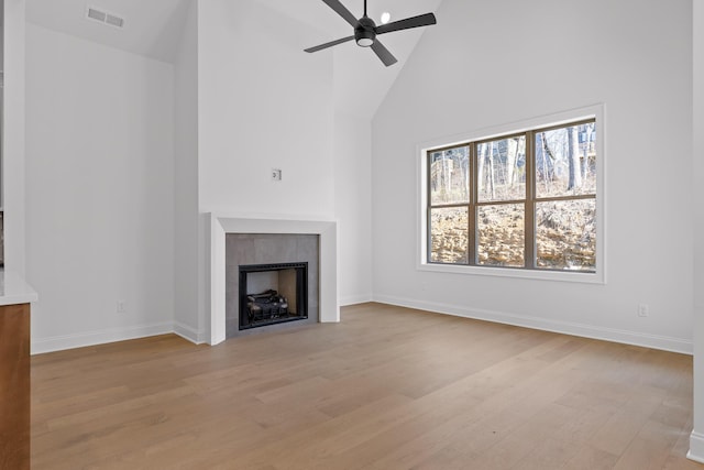 unfurnished living room with visible vents, a ceiling fan, a tiled fireplace, light wood-style floors, and high vaulted ceiling