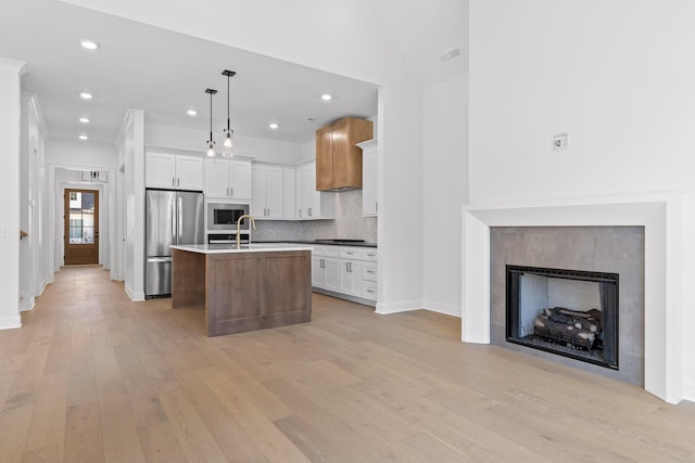 kitchen with light wood-style flooring, visible vents, appliances with stainless steel finishes, decorative backsplash, and an island with sink