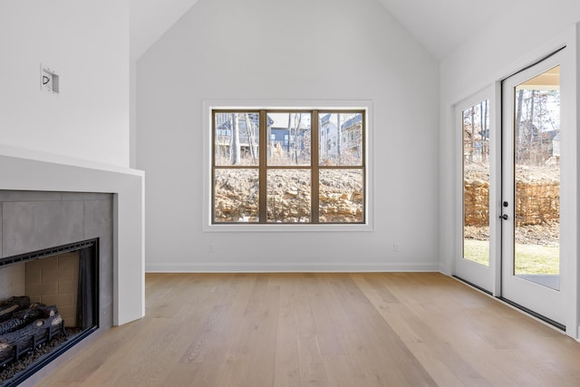 unfurnished living room with baseboards, vaulted ceiling, french doors, light wood-type flooring, and a fireplace