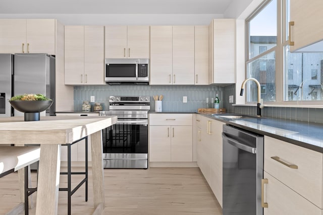 kitchen featuring dark countertops, light wood-style flooring, appliances with stainless steel finishes, a sink, and backsplash