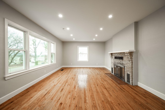 unfurnished living room with a healthy amount of sunlight, light hardwood / wood-style floors, and a brick fireplace