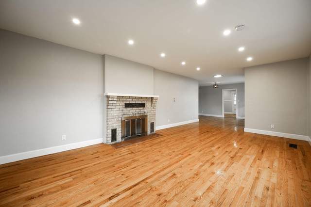 unfurnished living room with a brick fireplace and light wood-type flooring